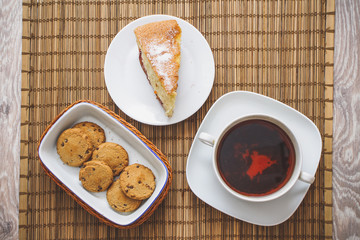Plum biscuit cake for a cup of hot tea on a straw bedding with chocolate biscuits in a basket.