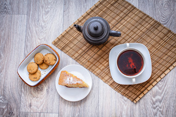 Biscuit plum cake on a plate with a cup of tea of hot space on a straw bedding chocolate chip cookies in a basket.