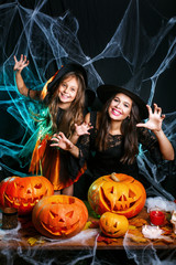 Cute little girl and her beautiful mom in witch hats and costumes are looking at camera and having...