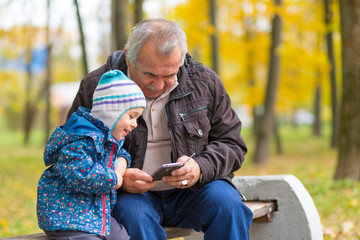 Fototapeta premium young boy in the park with his grandfather calls his parents. Happy family together.