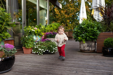 Fototapeta premium Little smiling boy runs on a terassa of cafe. Lovely kid smiles and has joy. Outdoor activities for children