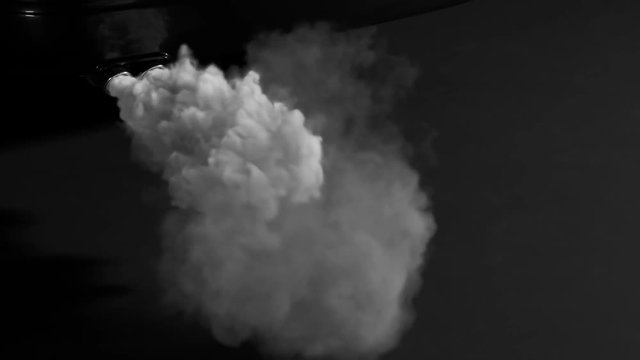 Fumes emmited from car exhaust dual pipe. White dense smoke on black background.