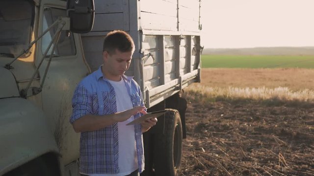 A pensive farmer is working in the field. Uses a tablet, stands near the agricultural engineering.