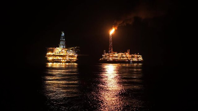 FPSO tanker vessel near Oil platform Rig. Offshore oil and gas industry, sea oil production and storage. Flare boom is brightly burning at night.