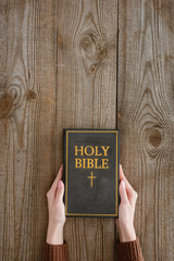 cropped shot of woman holding holy bible on wooden tabletop