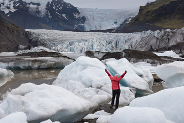 Active woman raising hands in front of the huge glacier in Iceland
