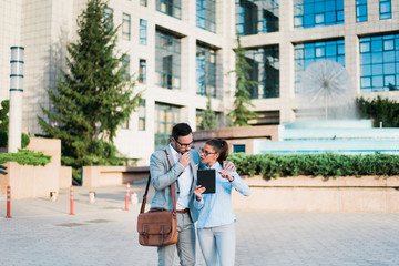 Team of two young successful smart modern attractive businessman and businesswoman in the city working together outside and discussing designer projects.