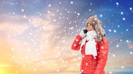 Fototapeta na wymiar people, season and leisure concept - happy smiling woman in winter fur hat calling on smartphone outdoors over sky background and snow