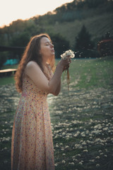 Happy beautiful woman blowing dandelion in the field