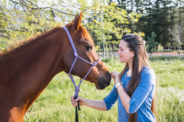 Teenage girl standing with her chestnut Arab horse interacting with him close up.