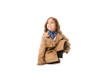 stylish little child in trench coat sitting on floor isolated on white