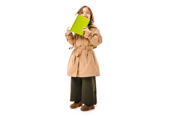 happy little child in trench coat with book looking at camera isolated on white