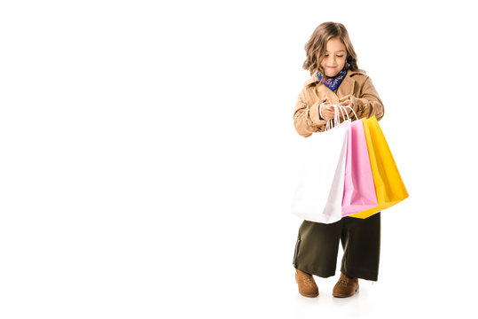 beautiful little child in trench coat holding colorful shopping bags isolated on white