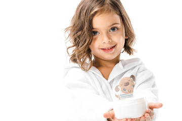 cute kid in white bathrobe showing body cream in hands isolated on white