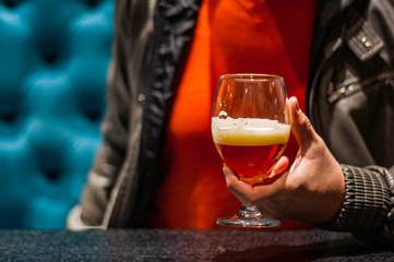 man's hand holds a glass of amber Pale Ale beer in bar