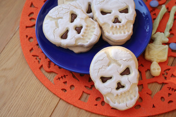 Halloween cookies filled with chocolate in shape of a skull on a plate on wooden table
