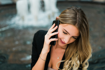 Beautiful blonde successful business woman sitting, talking on a phone and smiling, holding a business plan.