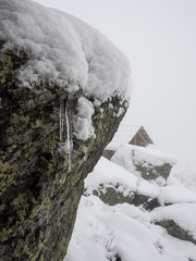 icicle on a rock during a snow storm. roof of a house with a snowdrift in the background