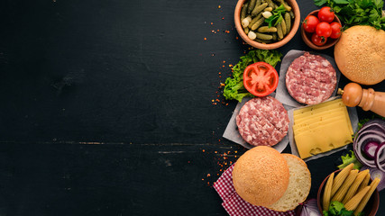 Preparation of burger. Meat, fresh vegetables, tomatoes, onions. On a black wooden background. Top view. Free copy space.