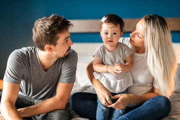 Family of three sit on the bed with 1 years child girl and cat