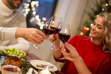 holidays and celebration concept - close up of happy friends having christmas dinner at home, drinking red wine and clinking glasses