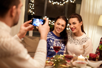 holidays and celebration concept - happy friends having christmas dinner at home and taking picture by smartphone