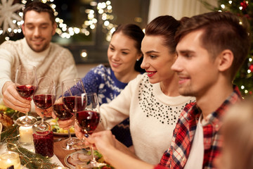 holidays and celebration concept - happy friends having christmas dinner at home, drinking red wine and clinking glasses