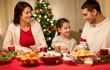 holidays, family and celebration concept - happy mother, father and little daughter having christmas dinner at home