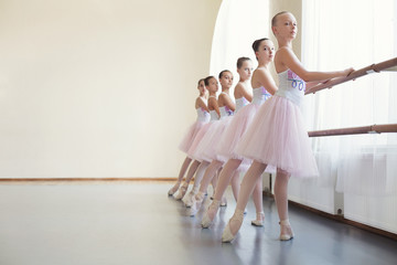 Young ballerinas rehearsing in ballet class, performing different exercises - obrazy, fototapety, plakaty