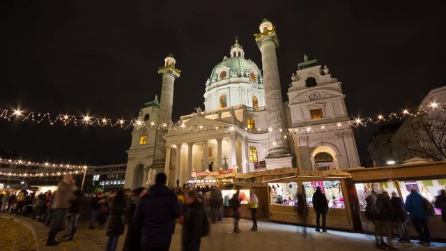 Famous Christkindlmarkt at Karlsplatz with crowd of tourists and people in festive mood in Christmas time. Karlskirche (St. Charles's Church) in background.