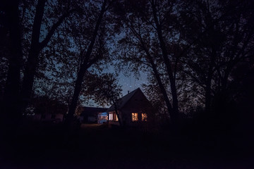 Small cozy house with luminous windows under the starry sky among the forest. night photo.
