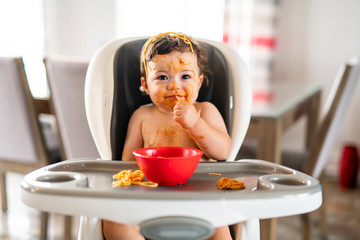 child girl, eating spaghetti for lunch and making a mess at home in kitchen