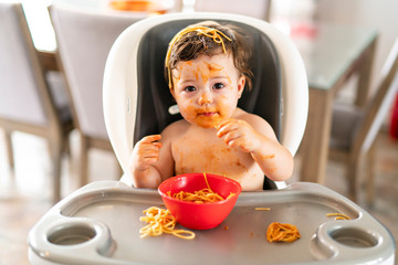 child girl, eating spaghetti for lunch and making a mess at home in kitchen