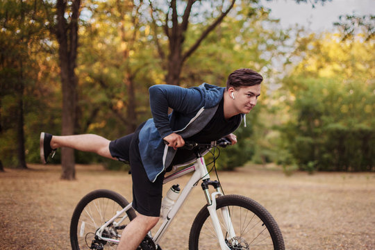 Attractive young caucasian man with dark hair bicycling in the park. White earphones, favorite music. Outdoors, golden leaves. Early autumn / fall background. Healthy life sport, fitness. Copy space