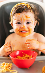 child girl, eating spaghetti for lunch and making a mess at home in kitchen