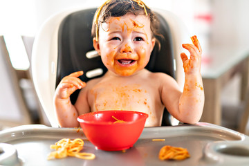 child girl, eating spaghetti for lunch and making a mess at home in kitchen