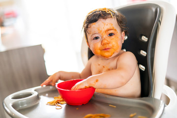 child girl, eating spaghetti for lunch and making a mess at home in kitchen