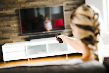 Young woman watching television sitting on the sofa at home. Back view