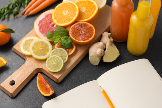 food, healthy eating and vegetarian concept - close up of citrus fruits on wooden cutting board, bottles of juices and notebook on slate table top