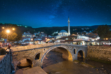 Night view of old stone bridge and old Ottoman Sinan Pasha Mosque in Prizren, Kosovo. Historic city located on the banks of the  Bistrica river, beautiful night landscape with star sky after sunset