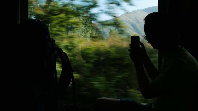 Man tourist photographs on a smartphone a mountain landscape from the train window, traveling by rail