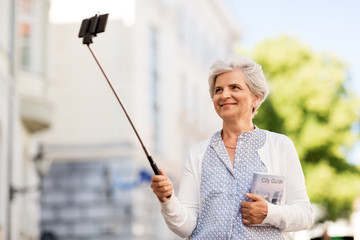 travel, tourism and retirement concept - happy senior woman taking picture by selfie stick on city street in summer