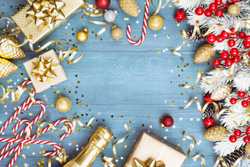 Christmas background with snowy fir tree, gift or present box, champagne and holiday decorations on blue wooden table top view. Greeting card with space for text.