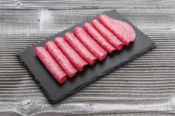 delicious sliced salami on a stone plate wooden background