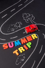 Toy car on the road and inscription plastic letters summer trip on chalkboard