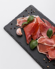 Italian prosciutto crudo or spanish jamon on a stone plate white background