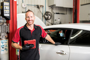 handsome mechanic based on car in auto repair shop with tablet on hand