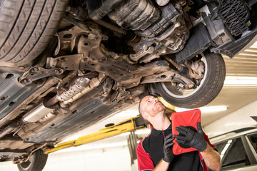 handsome mechanic based on car in auto repair shop with tablet on hand