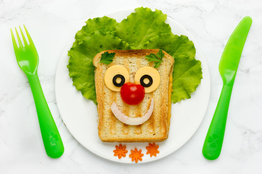 Funny clown face grilled sandwich with cheese and vegetables for kids lunch top view