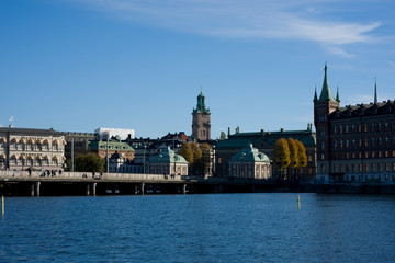 Fototapeta na wymiar Stockholm water front with landmarks, boats an autumn day with blu sky and sea, orange and red leafs.